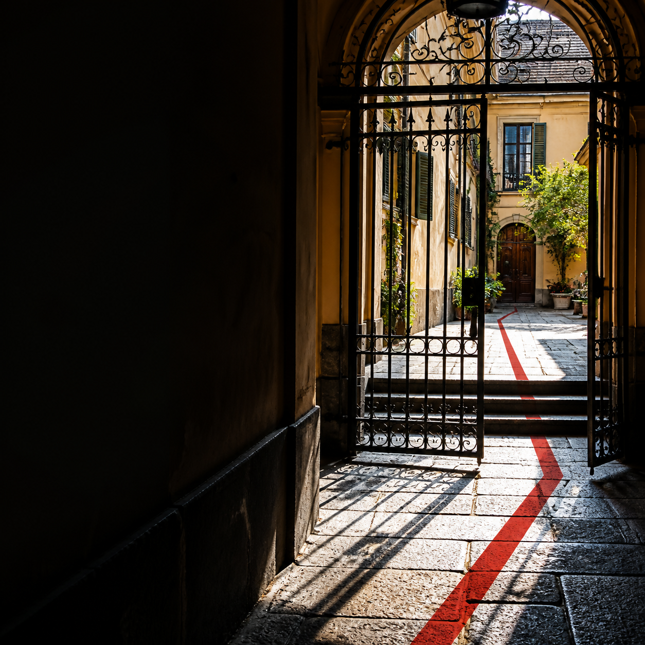Cancello pedonale e passaggio in un cortile condominiale italiano, con una sottile linea rossa sul pavimento come traccia editoriale.